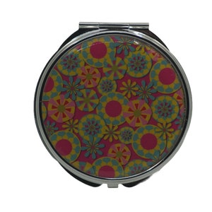 Puede incluir: Un espejo de bolsillo plateado con un diseño floral redondo, rosa, amarillo y azul.