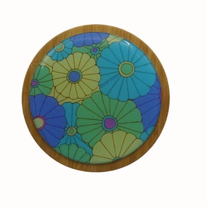 May include: A round wooden coaster with a colourful floral design. The coaster features a pattern of blue, green, and yellow flowers with a glossy finish.