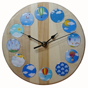 May include: A wooden clock with a light wood background and twelve colourful round images of hot air balloons, clouds, and sunshine. The clock hands are black.