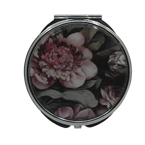 Puede incluir: Un espejo de bolsillo plateado con un diseño floral. El diseño presenta flores rosas y blancas sobre un fondo oscuro.