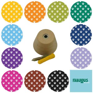 May include: A light-colored wooden wall hook with a conical shape, accompanied by a metal screw and a yellow plastic wall anchor. Surrounding the hook are eleven circular swatches featuring a repeating white paw print pattern on various colored backgrounds including yellow, orange, green, teal, blue, dark blue, purple, light purple, pink, brown, and black.
