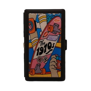Peut inclure: Porte-cartes noir avec un motif coloré de skateboard des années 1970. Le motif comprend un skateboard rose, le texte "The 1970s" et une main tenant un appareil photo. Le portefeuille a une fermeture magnétique.