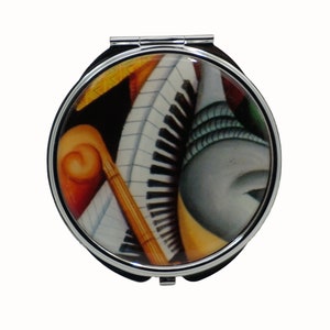 Puede incluir: Un espejo compacto plateado con un diseño colorido que presenta instrumentos musicales, incluyendo un piano, un saxofón y un violín. El diseño es abstracto y presenta una mezcla de naranja, amarillo, azul y negro.