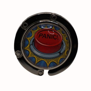 Peut inclure: Un porte-sac en métal argenté avec un bouton rouge sur lequel est inscrit "PANIC!" en lettres blanches. Le bouton est entouré d'un motif de style bande dessinée jaune et bleu.