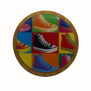 May include: A round wooden coaster featuring a colourful design of nine sneakers in a pop art style. The sneakers are in various colours, including red, blue, green, yellow, orange, pink, and black.