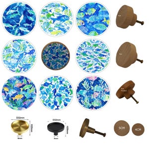 May include: A selection of cabinet knobs and drawer pulls with aquatic themes. The knobs display watercolour fish designs in blue, green, and yellow. Also shown are wooden knobs and metal knobs with dimensions in cm.