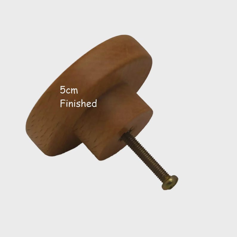 May include: A round, light brown wooden cabinet knob with a smooth, finished surface. The knob features a cylindrical base and a metal screw extending from the centre. Text printed on the surface of the wood reads 5cm Finished.