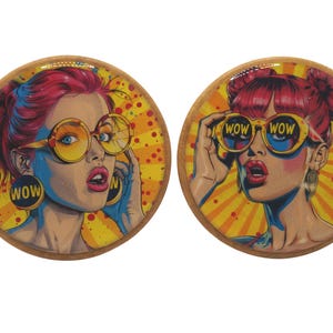 Puede incluir: Dos posavasos redondos con diseño pop art. Cada posavasos presenta a una mujer con cabello rojo y gafas de sol amarillas. La palabra "WOW" se muestra en los pendientes y gafas de sol. El fondo es amarillo y naranja.