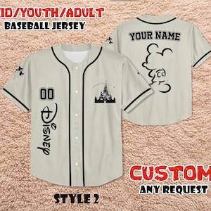 May include: A beige baseball jersey with black trim, featuring the word "Disney" in black script, the number "00", and a castle silhouette. The back of the jersey has a Mickey Mouse outline and the text "YOUR NAME".