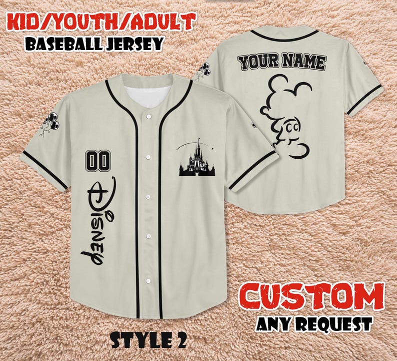 May include: A beige baseball jersey with black trim, featuring the word "Disney" in black script, the number "00", and a castle silhouette. The back of the jersey has a Mickey Mouse outline and the text "YOUR NAME".