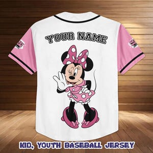 May include: White baseball jersey with pink sleeves and black trim. Features a Minnie Mouse graphic on the back, with the text "YOUR NAME" above the graphic. The text "KID, YOUTH BASEBALL JERSEY" is at the bottom.