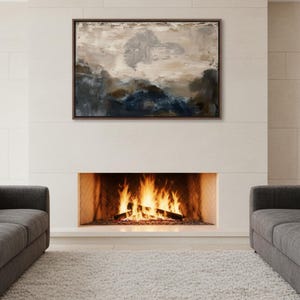 Pode incluir: Uma pintura abstrata de paisagem em uma moldura de madeira escura está pendurada acima de uma lareira com fogo. Dois sofás cinzentos estão em ambos os lados da lareira, e um tapete branco cobre o chão. A pintura apresenta tons de azul, castanho e bege.