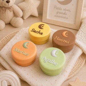 May include: Four round silicone containers in yellow, brown, orange, and light green. Each lid features a raised crescent moon and star icon with a personalised name: Sacha, Naomi, Marius, and Agathe, written in a script font on the top surface.