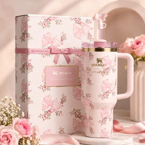 May include: A pink Stanley Loveshack Fancy tumbler and gift box set. The tumbler and box feature a floral and bow pattern. The tumbler has a handle and a straw. The gift box is tied with a pink ribbon.