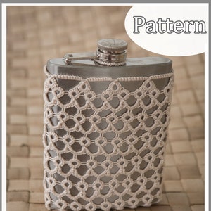 May include: A silver flask with a white crocheted cover. The cover has a diamond pattern. The flask is sitting on a woven surface.