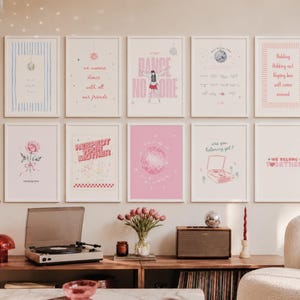 May include: A collection of framed art prints with various designs and text, including phrases like "Dance No More" and "Respect Your Mother." The prints are in white frames and are displayed on a wall above a wooden console with a record player and speakers.
