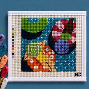 May include: A square needlepoint canvas featuring a colorful abstract design with green, orange, and pink geometric shapes on a blue background. A column of color swatches is on the left, and the initials NC are in the bottom right corner. Eight skeins of embroidery floss in various colors are arranged vertically on the left side.