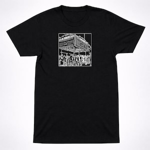 May include: Black t-shirt featuring a white graphic of a concert marquee with the text "M. CONCERT" and "Sunny day real estate LIVE". The graphic shows a crowd of people in front of the marquee.