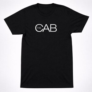 May include: Black crew neck t-shirt with the white text "THE CAB" printed across the chest. The text is in a sans-serif font. The shirt is made of a soft material.