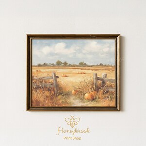 May include: A framed landscape painting shows a field of pumpkins and tall grass under a cloudy sky. A wooden fence leads into the scene. The artwork is in a gold-coloured frame.