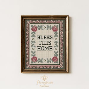 Könnte beinhalten: Gerahmtes Kreuzstich-Kunstwerk mit den Worten "BLESS THIS HOME". Das Design umfasst einen floralen Rahmen mit roten Rosen und grünen Blättern, vor einem cremefarbenen Hintergrund. Der Rahmen hat eine dunkelbraune Farbe.