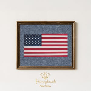 May include: Framed print of the American flag. The flag features red and white stripes and a blue field with white stars. The flag is set against a denim-like background and framed in a brown wooden frame. The print is from Honeybrook Print Shop.