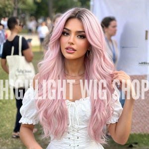 Può includere: Una parrucca lunga e ondulata rosa pastello con una transizione di radici scure, acconciata con una riga centrale e strati voluminosi. Il testo "HIGHLIGHT WIG SHOP" è sovrapposto in lettere maiuscole bianche al centro dell'immagine.