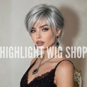 May include: A woman with short, silver-gray hair and a black lace top. She wears a silver necklace and earrings. The text "HIGHLIGHT WIG SHOP" is displayed in large white letters across the image.