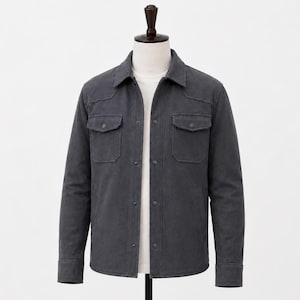 May include: A charcoal grey long-sleeve shirt jacket featuring a classic collar, a button-down front with matching buttons, and two chest pockets with buttoned flaps. The garment is displayed on a mannequin over a plain white t-shirt.
