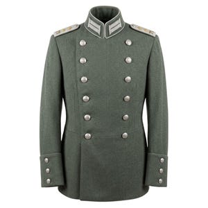 Puede incluir: Chaqueta de estilo militar, cruzada, en color verde apagado. La chaqueta presenta botones plateados, charreteras y un cuello alto con ribetes blancos y plateados. Las mangas tienen puños abotonados. La chaqueta está entallada y parece estar hecha de un material similar a la lana.