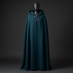 May include: A floor-length, deep teal hooded cloak featuring a structured hood and a single wooden toggle closure at the neck. The garment is made of a solid-colored, textured fabric that drapes down to the floor in a full, flowing silhouette.
