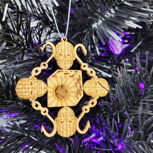May include: Wooden Christmas ornament featuring a cube with four faces depicting a human head with a grid pattern. The cube is surrounded by chains and hooks.