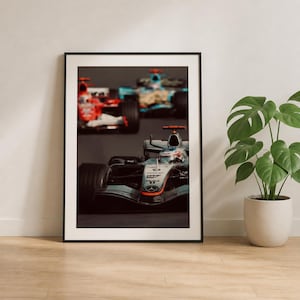 Peut inclure: Impression encadrée représentant trois voitures de course de Formule 1 en action. La voiture de tête est argentée avec des pneus noirs et des détails orange. Les autres voitures sont rouges et bleues.