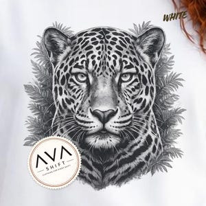 May include: A white t-shirt featuring a detailed black and white illustration of a leopard head surrounded by fern leaves. The text "WHITE" appears in the upper right corner, and a circular logo with the text "AVA SHIFT CLOTHING FOR EVERY SHIFT" is visible.