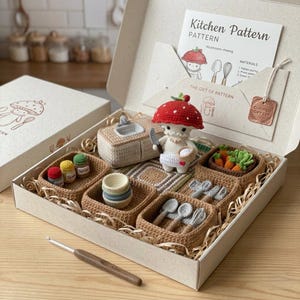 Op de afbeelding: Een haakpakket in een doos met een paddenstoelfiguur, een gootsteen, kruidenpotjes, een mandje met wortels en keukengerei. De set bevat een geprinte patroonkaart met de titel Kitchen Pattern en een haaknaald van 4,0 mm.