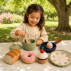 May include: A collection of crocheted play food and kitchen items including a sage green pot with a lid and spoon, a black frying pan with a colorful egg, a loaf of bread, a pink frosted donut, a cupcake with a cherry, and a floral plate.