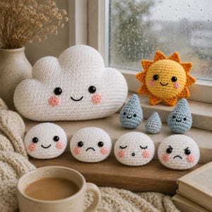 Può includere: Una collezione di oggetti all'uncinetto che include una grande nuvola bianca, un sole giallo, tre gocce di pioggia azzurre e quattro piccole figure circolari bianche con varie espressioni facciali, tra cui felice, triste, sorpreso e arrabbiato.
