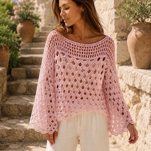 Può includere: Un top all'uncinetto rosa chiaro con maniche a campana ampie e scollatura rotonda. Il motivo a trama aperta è visibile. Il top è abbinato a pantaloni bianchi con coulisse, creando un look rilassato ed estivo.