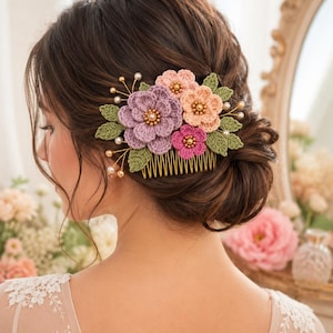 以下が含まれることがあります： 紫、桃色、ピンクの色合いの、かぎ針編みの花が特徴のフローラルヘアコーム。緑の葉と金色のワイヤーとコームでアクセントをつけました。コームは小さな真珠で飾られており、エレガントなアクセサリーです。