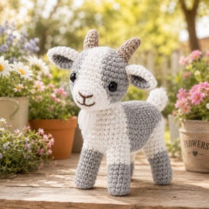 May include: A crocheted stuffed goat toy featuring a white and grey color scheme, two small tan horns, black safety eyes, a stitched nose and mouth, and a small white beard. The plush animal stands on four legs with a short tail and textured yarn.
