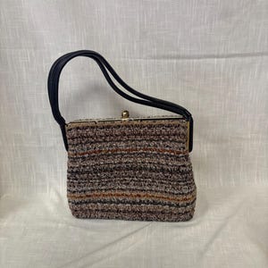 May include: A vintage handbag with a textured, multi-colored exterior in shades of brown, gray, and orange. The bag features a black handle and a gold-toned clasp. The bag's design is rectangular with a structured shape.