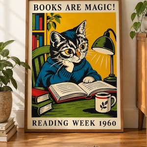 May include: A framed poster featuring a cat in a blue sweater reading a book at a desk with a green lamp, a mug, and stacked books. The text reads BOOKS ARE MAGIC! and READING WEEK 1960. The illustration uses a yellow background and bold colors.