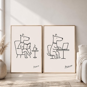 Puede incluir: Dos láminas de arte mural enmarcadas con dibujos de líneas negras sobre fondo claro. La lámina de la izquierda muestra a un perro sentado en una silla leyendo un libro junto a una taza de café. La de la derecha muestra a un perro sentado en un escritorio usando un portátil. Ambas llevan la firma Picasso.