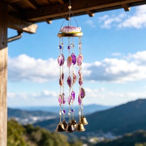 Puede incluir: Un carillón de viento colgante con cristales de amatista y campanas de latón. La sección superior tiene un gran grupo de amatistas, con hebras de cristales morados y transparentes colgando debajo. Pequeñas campanas de latón en la parte inferior.
