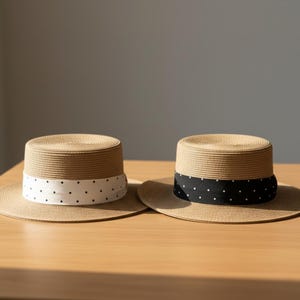 May include: Two straw boater hats with wide brims and cylindrical crowns. One hat has a white band with black polka dots, and the other has a black band with white polka dots. Both hats sit on a wooden surface.