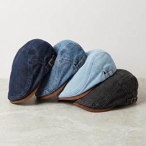 May include: A collection of four flat caps in varying shades of denim, including dark blue, medium blue, light blue, and charcoal gray. Each cap features a structured crown, a short stiff brim, and a small adjustable metal buckle on the side.