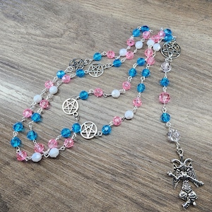May include: A rosary with blue, pink, and white beads, connected by silver-toned metal chains. The rosary features pentagram charms and a detailed pendant of a horned figure.