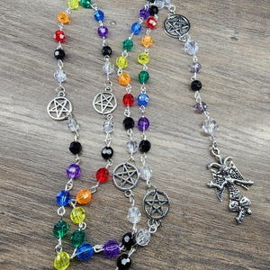 May include: A colorful rosary with rainbow-colored beads and silver pentagram charms. The rosary features a silver pendant of a horned deity. The beads are arranged in a traditional rosary pattern.