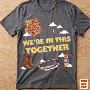 Op de afbeelding: Een donkergrijs t-shirt met een grafische print van een bruine sheriffster met de tekst Marshall To The Stars & Beyond, de tekst WE'RE IN THIS TOGETHER, bruine cowboylaarzen, een kleurrijke kralenarmband met de tekst SIDE BY SIDE en blokken.