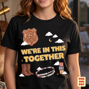 Op de afbeelding: Een zwart t-shirt met een grafische print van een bruine sheriffbadge met de tekst Marshall's To The Stars & Beyond, de tekst WE'RE IN THIS TOGETHER, bruine cowboylaarzen, een kralenarmband met SIDE BY SIDE en alfabetblokken.